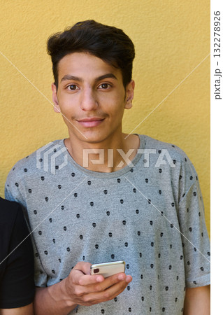 Middle Eastern Teenager Using Mobile Phone While Leaning Against Yellow Wall Middle Eastern Teenager Using Mobile Phone While Leaning Against Yellow Wall 132278926