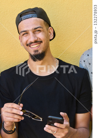 Close Up Portrait of Smiling Sudanese Teenager with Broad Smile, Chin, and Cap Using Smartphone  132278933
