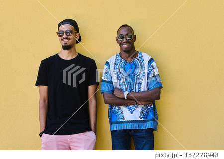 Two Male Friends: African American Teenager in Sudanese Traditional Attire Leaning Against Yellow Wall 132278948