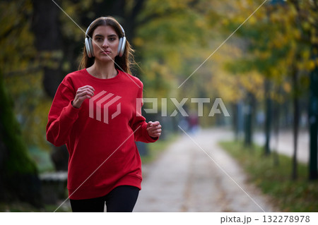 Young beautiful woman running in autumn park and listening to music with headphones on smartphone 132278978