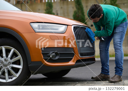 A man meticulously washes and cleans his car in the driveway of his home, showcasing pride in his vehicle and outdoor space. 132279001