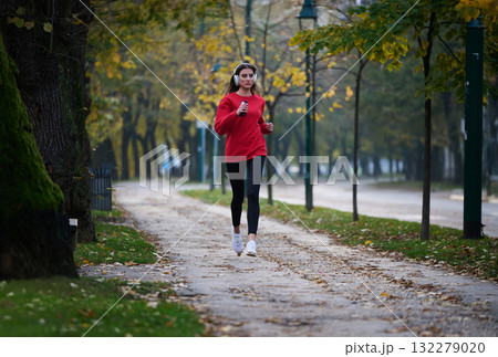 Young beautiful woman running in autumn park and listening to music with headphones on smartphone Young beautiful woman running in autumn park and listening to music with headphones on smartphone 132279020
