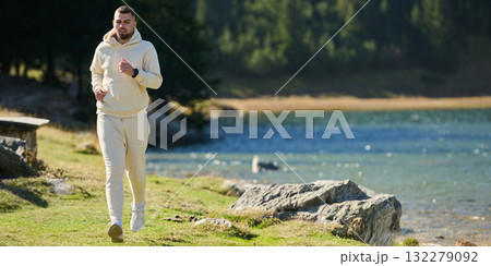 Athletic man maintains his healthy lifestyle by running through the scenic mountain and lakeside environment, showcasing a commitment to fitness and well-being Athletic man maintains his healthy lifestyle by running through the scenic mountain and lakeside environment, showcasing a commitment to fitness and well-being 132279092