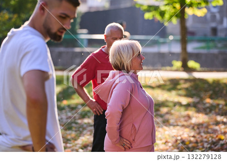 A group of seniors follows a trainer, engaging in outdoor exercises in the park, as they collectively strive to maintain vitality and well-being, embracing an active and health-conscious lifestyle in 132279128