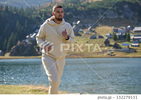 Athletic man maintains his healthy lifestyle by running through the scenic mountain and lakeside environment, showcasing a commitment to fitness and well-being Athletic man maintains his healthy lifestyle by running through the scenic mountain and lakeside environment, showcasing a commitment to fitness and well-being 132279131