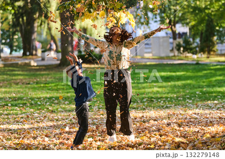 A modern woman joyfully plays with her son in the park, tossing leaves on a beautiful autumn day, capturing the essence of family life and the warmth of mother-son bonding in the midst of the fall A modern woman joyfully plays with her son in the park, tossing leaves on a beautiful autumn day, capturing the essence of family life and the warmth of mother-son bonding in the midst of the fall 132279148