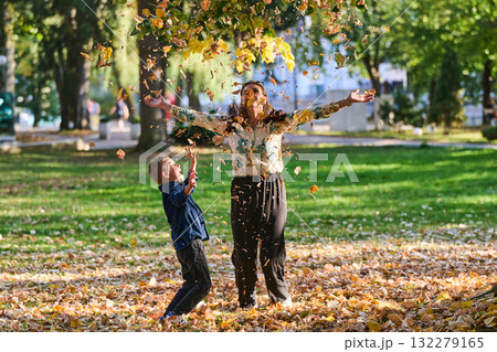 A modern woman joyfully plays with her son in the park, tossing leaves on a beautiful autumn day, capturing the essence of family life and the warmth of mother-son bonding in the midst of the fall A modern woman joyfully plays with her son in the park, tossing leaves on a beautiful autumn day, capturing the essence of family life and the warmth of mother-son bonding in the midst of the fall 132279165
