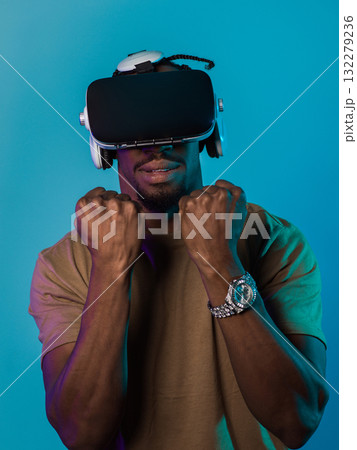 In an avant-garde scene, an African American man engages in cutting-edge virtual reality gaming, utilizing VR glasses to immerse himself in futuristic boxing games, set against a vivid blue background In an avant-garde scene, an African American man engages in cutting-edge virtual reality gaming, utilizing VR glasses to immerse himself in futuristic boxing games, set against a vivid blue background 132279236
