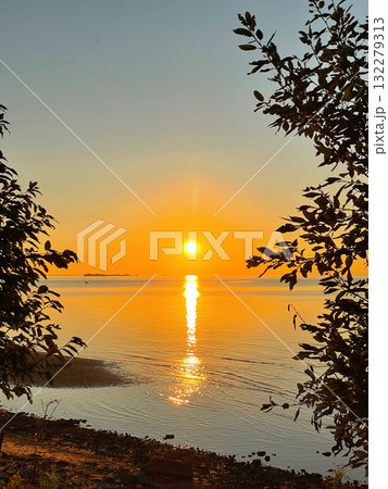 View of sunset over the sea through the tree branches. The sun sets on the water. The sky is painted with bright colors. Sunset beach in summer evening. Vertical photography. View of sunset over the sea through the tree branches. The sun sets on the water. The sky is painted with bright colors. Sunset beach in summer evening. Vertical photography. 132279313