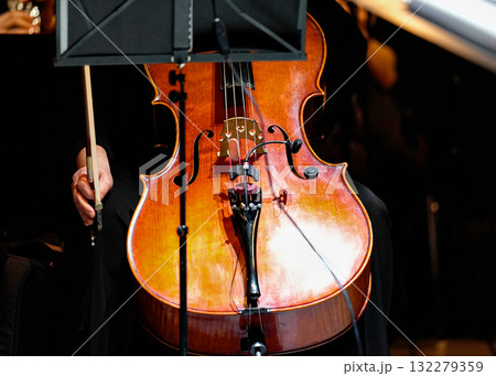 Cello front view showing wooden body bridge and strings with bow hand 132279359