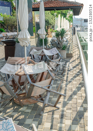 Stacked Wooden Chairs Rest Against Tables in a Serene Outdoor Restaurant 132280514