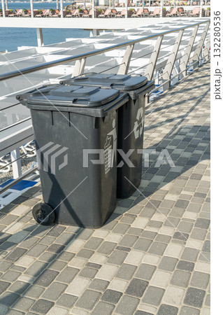 Trash and Recycling Bins Placed Along a Waterfront Promenade in Bright Daylight Trash and Recycling Bins Placed Along a Waterfront Promenade in Bright Daylight 132280536