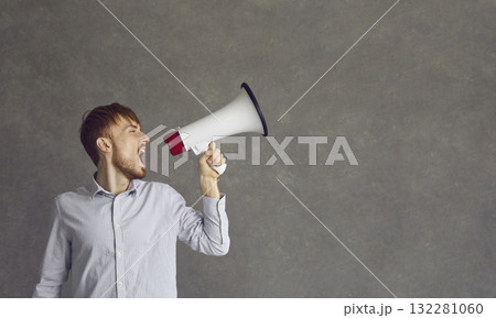 Young determined man makes a loud announcement while speaking into a loudspeaker. 132281060