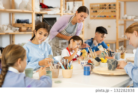 Children painting ceramics with a teacher Children painting ceramics with a teacher 132282838