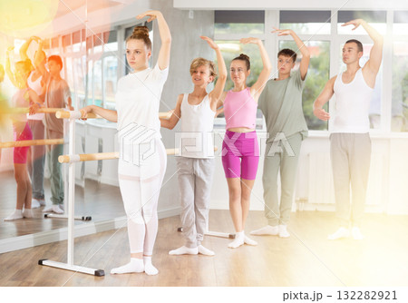 Girls and boys in ballet class perform third position under male teacher guidance. 132282921