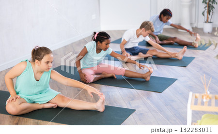 Diligent children practicing hand to toe pose of yoga on black mat in light room 132283011
