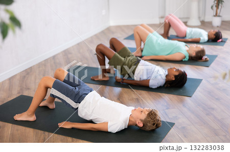 In sport studio with group of friends, boy perform bridge pose, setu bandha sarvangasana 132283038