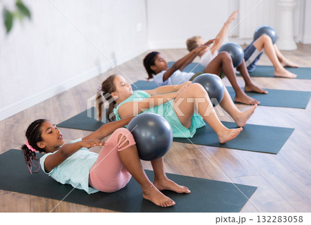 Portrait of childrens with pilates balls, pumping press during group class in fitness studio 132283058