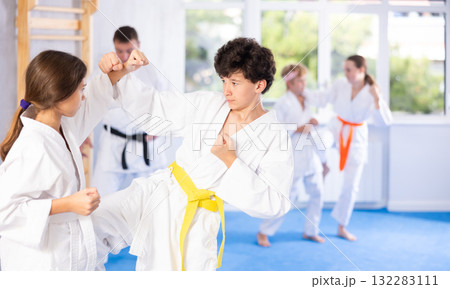 Teenagers girl and boy in kimono sparring together in gym during karate training Teenagers girl and boy in kimono sparring together in gym during karate training 132283111
