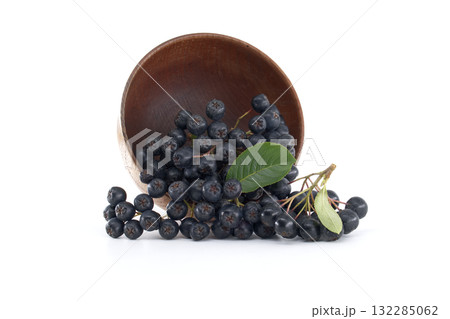 A group of aronia berries spills from a wooden bowl, isolated against a white backdrop. A group of aronia berries spills from a wooden bowl, isolated against a white backdrop. 132285062