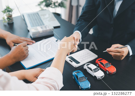 Business handshake after signing car loan contract, symbol of trust and successful auto finance agreement with money, calculator and vehicle model on desk, concept of deal and partnership. car loan. 132286277