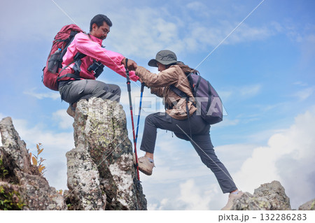 Two hikers on rocky mountain peak helping each other climb, symbol of teamwork, leadership, support, adventure, success, trust, exploration and outdoor lifestyle motivation in nature. 132286283