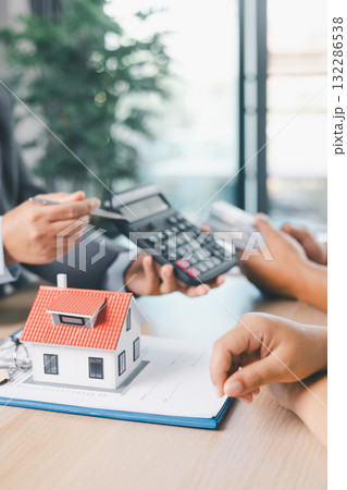 Close up of business people discussing mortgage loan with calculator, house model and contract paperwork on desk, concept of real estate finance, home ownership and property investment planning. 132286538