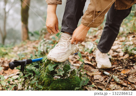 Close up of hiker tying shoelaces on sneaker with trekking pole in forest, symbol of preparation, adventure, outdoor lifestyle, hiking, journey and exploration in nature trail. adventure hiking Close up of hiker tying shoelaces on sneaker with trekking pole in forest, symbol of preparation, adventure, outdoor lifestyle, hiking, journey and exploration in nature trail. adventure hiking 132286612