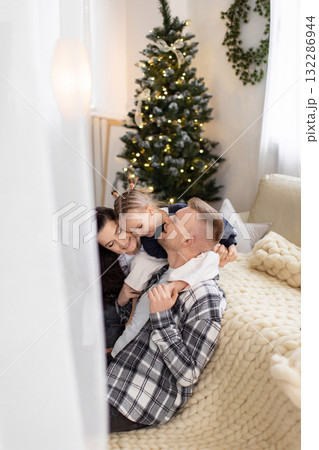 A happy family celebrates Christmas together in a cozy, decorated living room, embracing and smiling. 132286944
