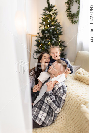 A happy family poses together in front of a Christmas tree, creating a warm and festive holiday scene. 132286945