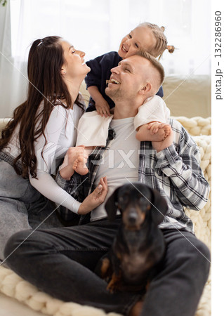 A joyful family, including a dog, shares a heartwarming moment of laughter and togetherness indoors. A joyful family, including a dog, shares a heartwarming moment of laughter and togetherness indoors. 132286960