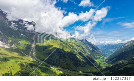 Majestic Alpine Valley Vista Lush Greenery, Towering Mountains, and Dramatic Cloudscape 132287317