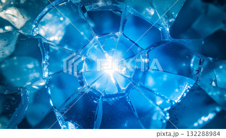 A macro view of shattered blue ice with a bright light shining through the geometric cracks, creating a dynamic and abstract winter background. 132288984