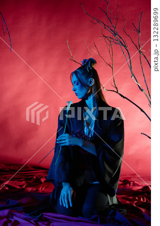 Woman in traditional Japanese dress poses with a flower in a vibrant studio setting Woman in traditional Japanese dress poses with a flower in a vibrant studio setting 132289699