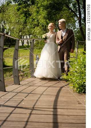 Couple walks hand in hand over bridge in sunny outdoor wedding celebration Couple walks hand in hand over bridge in sunny outdoor wedding celebration 132289708