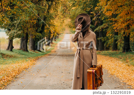 European woman in coat and hat walks along  yellow autumn trees 132291019