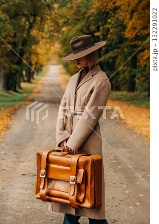 European woman in coat and hat walks along  yellow autumn trees 132291022