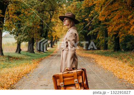 European woman in coat and hat walks along  yellow autumn trees 132291027
