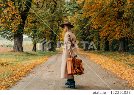 European woman in coat and hat walks along  yellow autumn trees 132291028