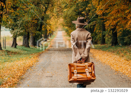 European woman in coat and hat walks along  yellow autumn trees 132291029