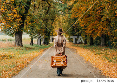 European woman in coat and hat walks along  yellow autumn trees 132291030