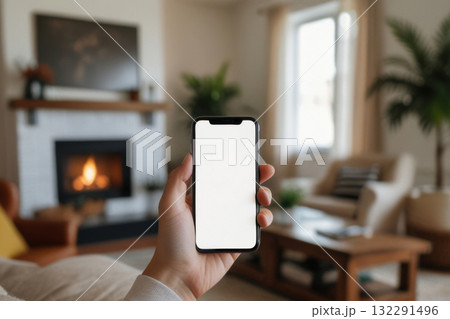 Hand holding a smartphone with a blank white screen in a softly living room Hand holding a smartphone with a blank white screen in a softly living room 132291496