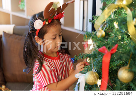 Festive Spirit. Young girl decorating Christmas tree with ornaments. Festive Spirit. Young girl decorating Christmas tree with ornaments. 132291694