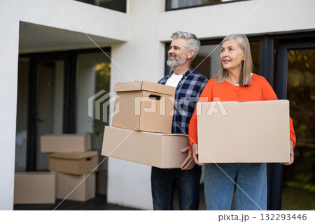 Mature couple holding moving boxes smiling at front door of house 132293446