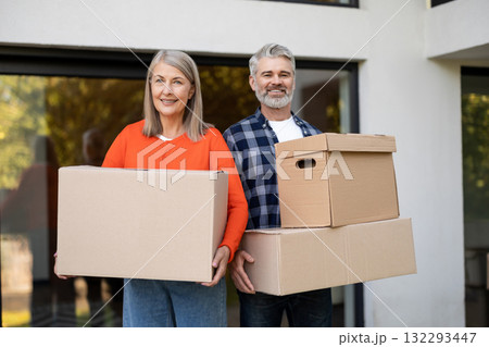 Smiling senior couple carrying cardboard boxes at home entrance 132293447