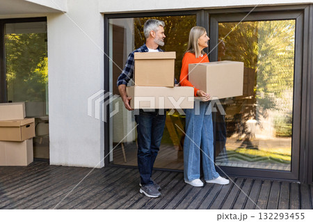 Happy senior couple managing home move carrying boxes together Happy senior couple managing home move carrying boxes together 132293455