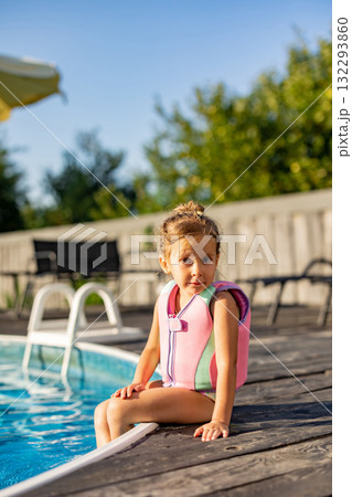 Cute kid in life jacket sitting on the swimming pool edge 132293860