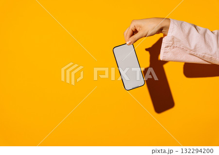 Hand holding modern smartphone with blank screen on vibrant yellow background Hand holding modern smartphone with blank screen on vibrant yellow background 132294200