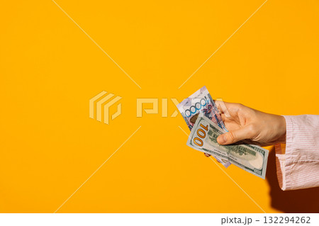 Female hand holding US dollars and Kazakh tenge on yellow Female hand holding US dollars and Kazakh tenge on yellow 132294262