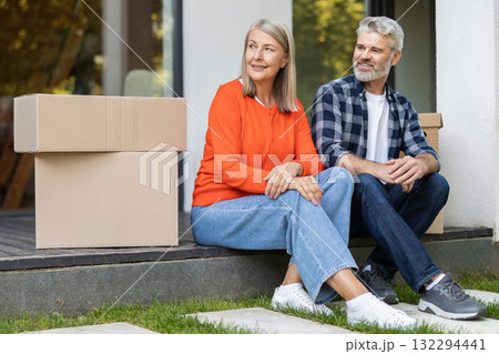 Happy senior couple sitting outside home near moving boxes Happy senior couple sitting outside home near moving boxes 132294441